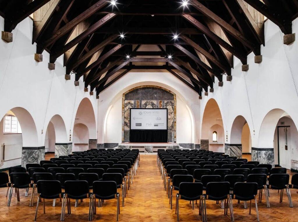 The main hall in theatre layout, with rows of seating facing the stage beneath exposed timber roof trusses